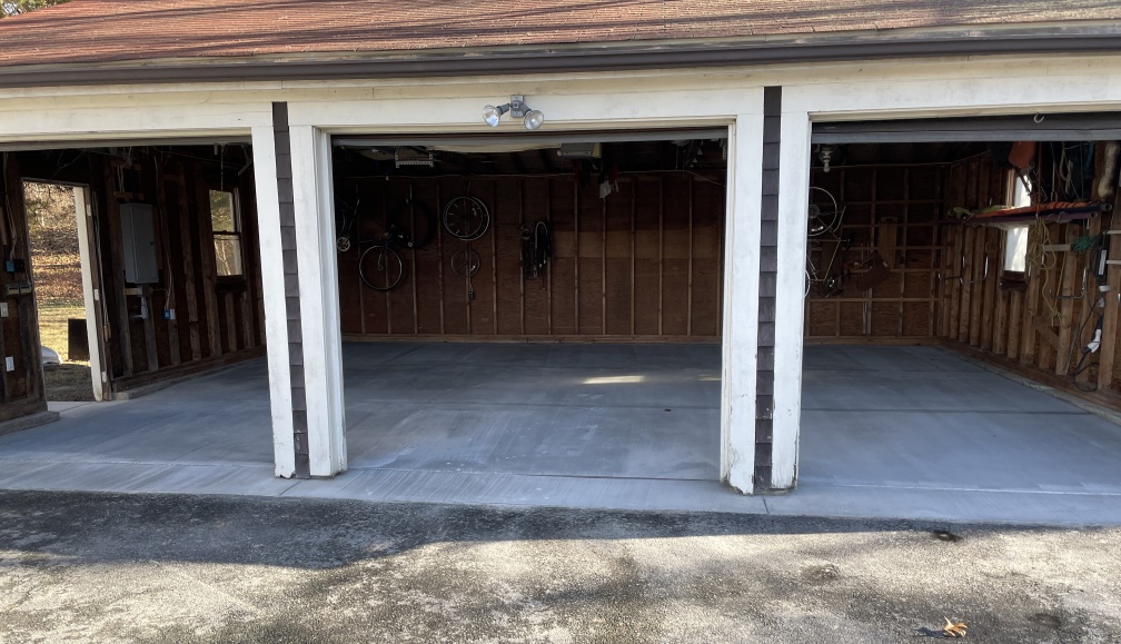 Shot encompassing all three bays of the garage, the cement is dried and lighter color now. The dark gray asphalt of the driveway is stained with light gray cement juice.